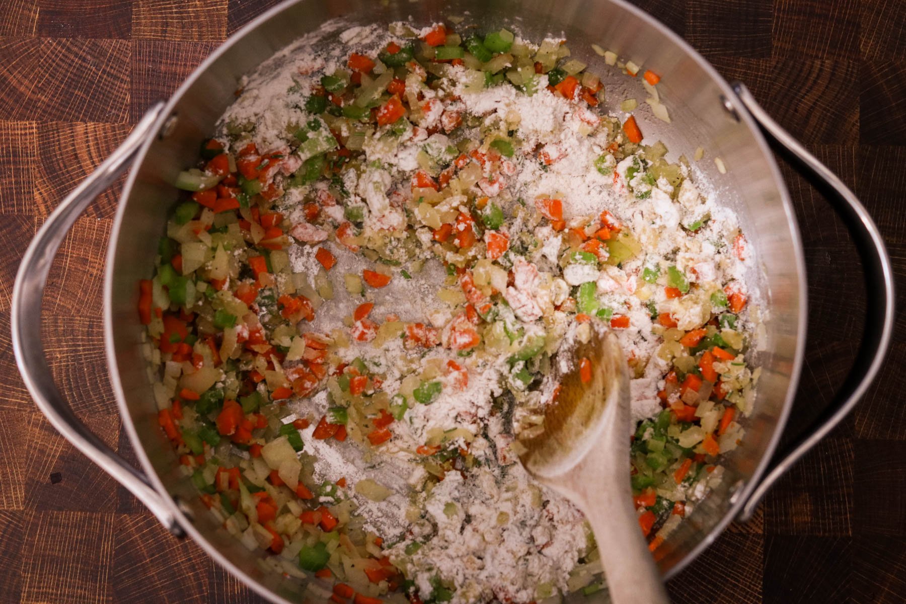Garlic, flour, rosemary, and thyme being stirred into the sautéed vegetables. 