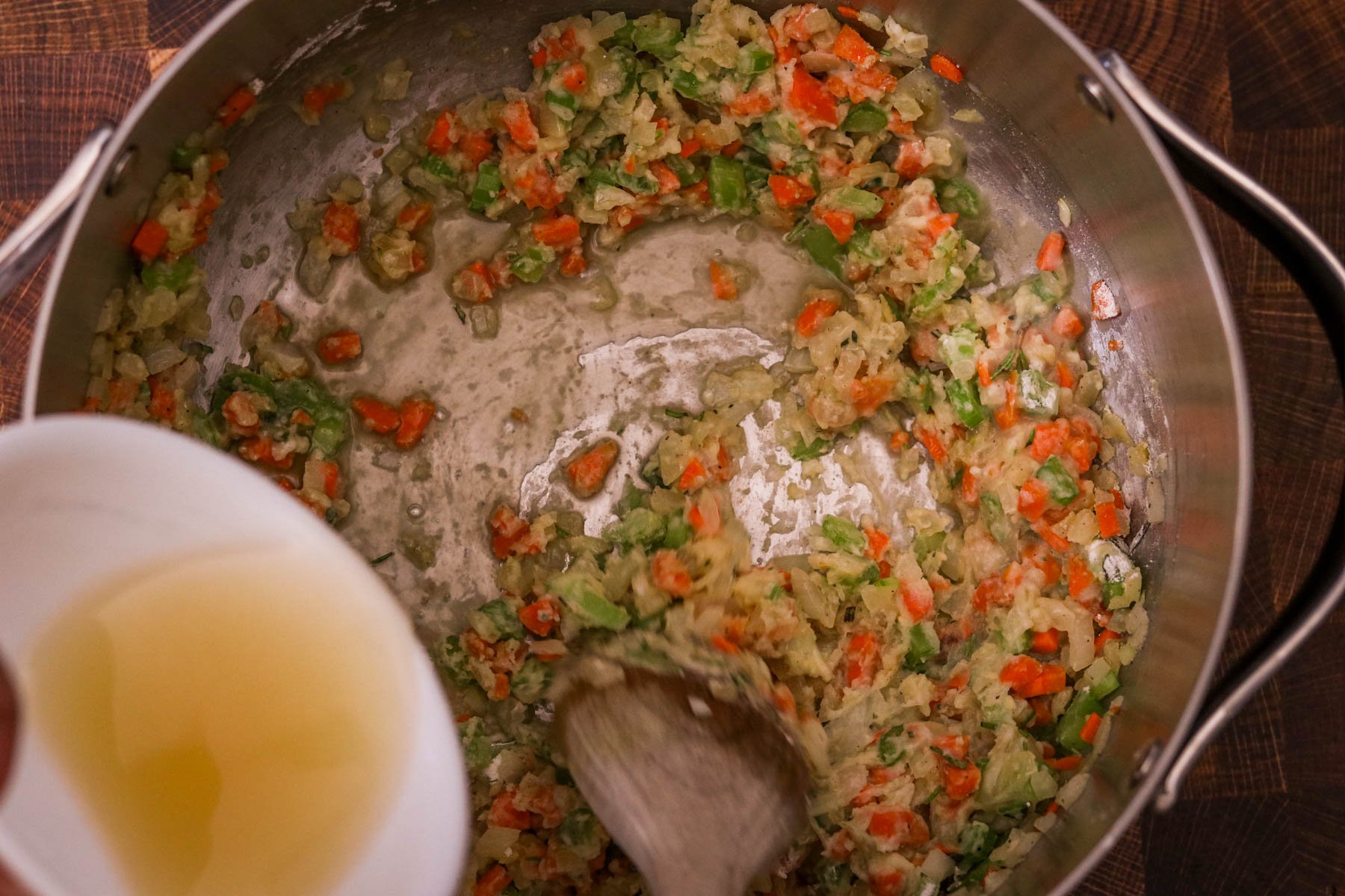 Broth being poured into the pot with sautéed vegetables, flour, and herbs.