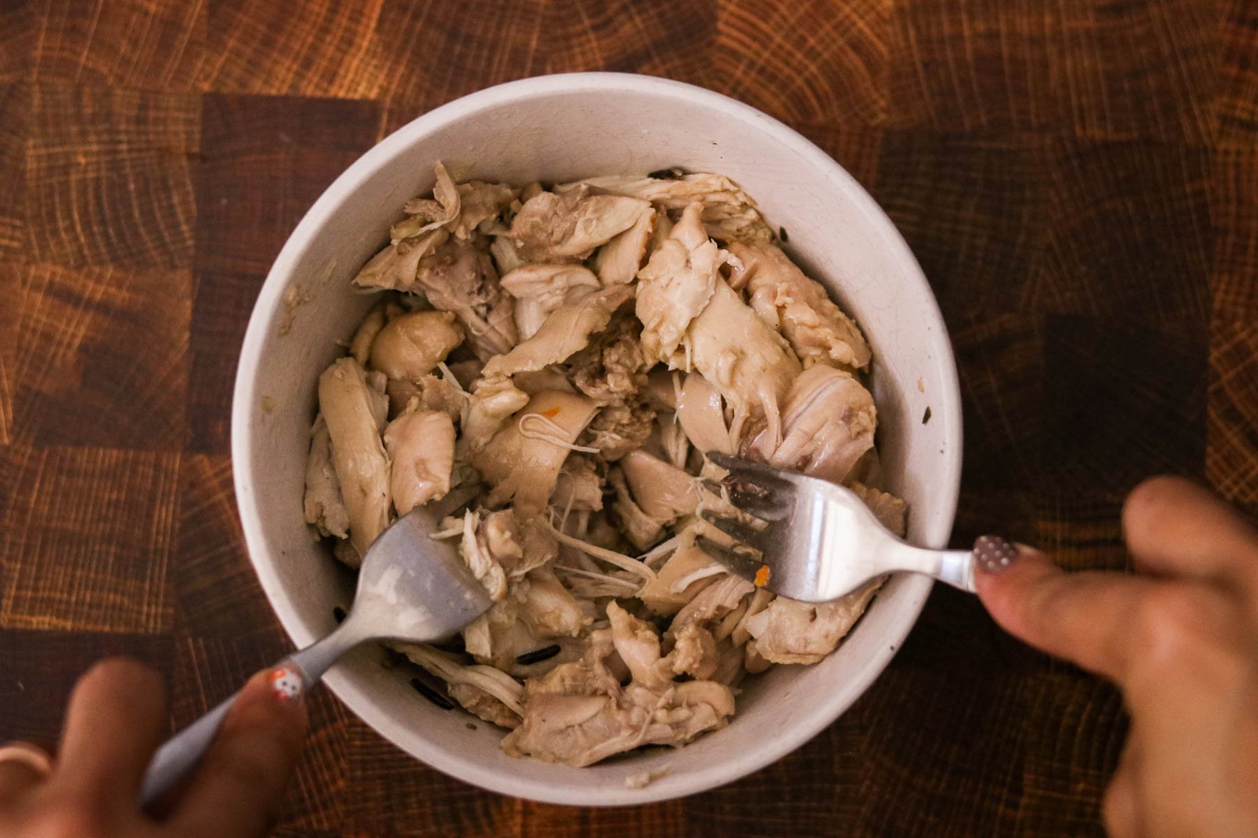 Cooked chicken in a small bowl being shredded with two forks.