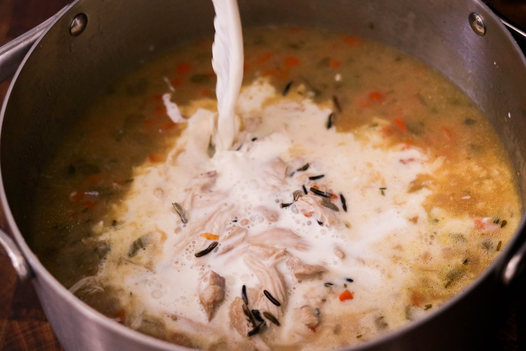 Milk being poured into the large pot of soup.