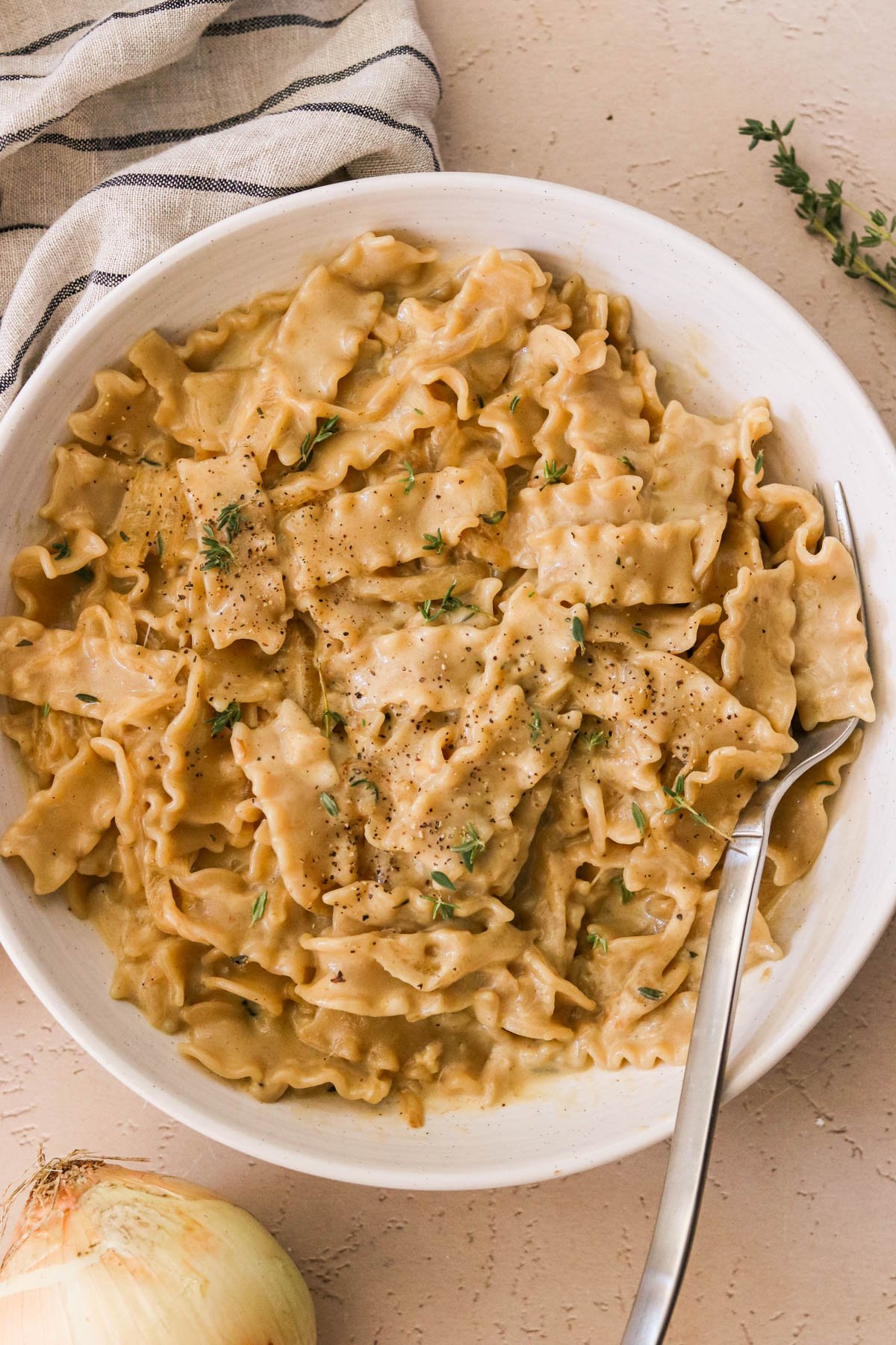 Creamy French onion pasta in a bowl, topped with melted cheese, pepper, and fresh thyme.