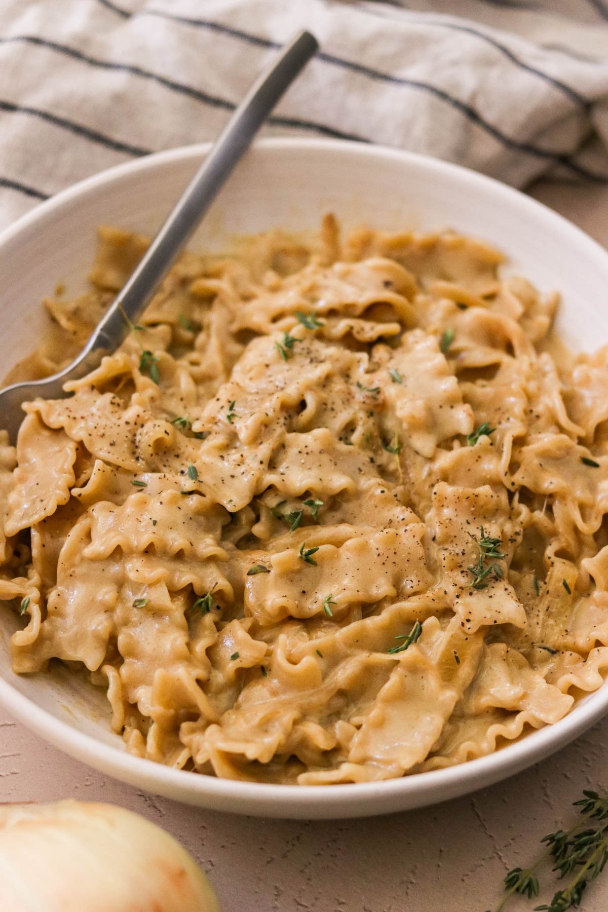 Close-up of cheesy French onion pasta with pepper and fresh thyme sprigs.
