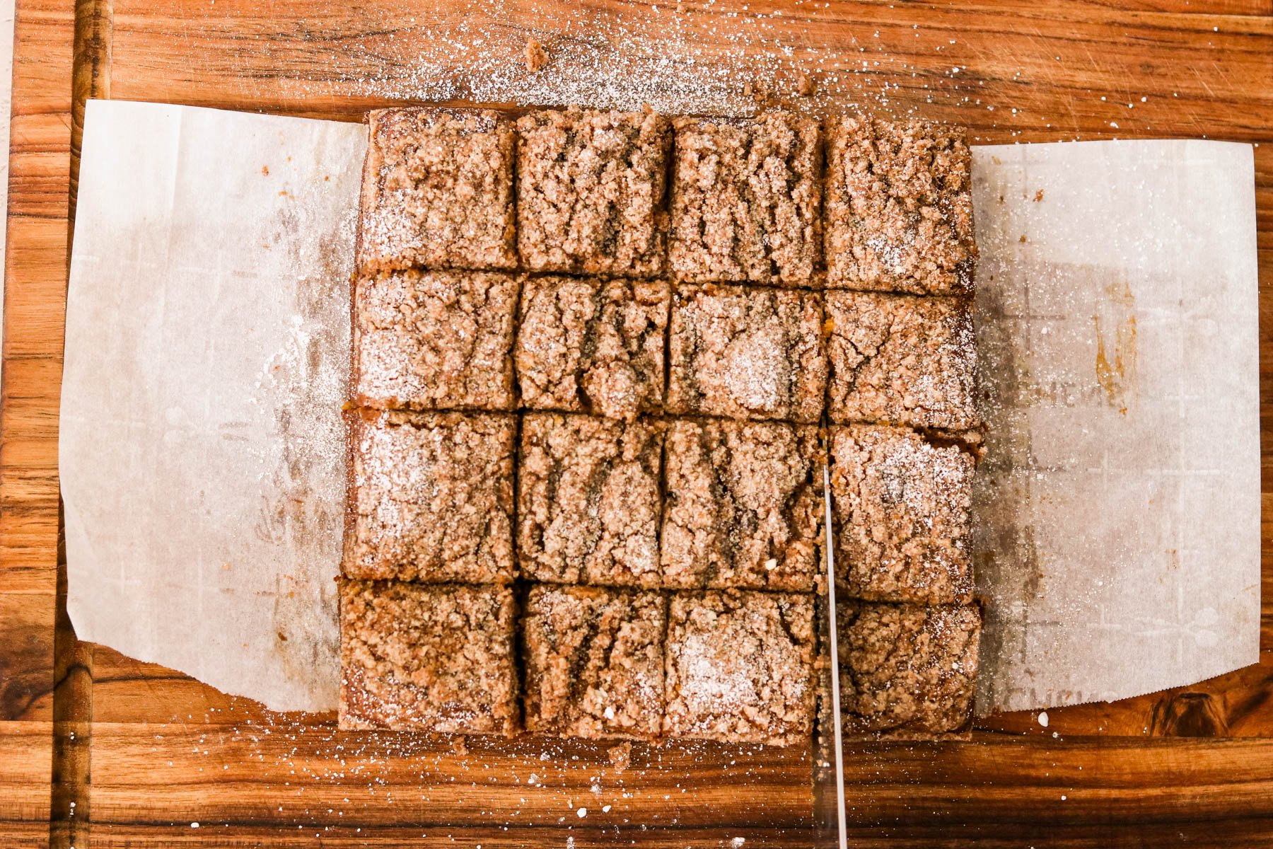 Sliced pumpkin coffee cake on parchment paper atop a wooden cutting board after cooling.