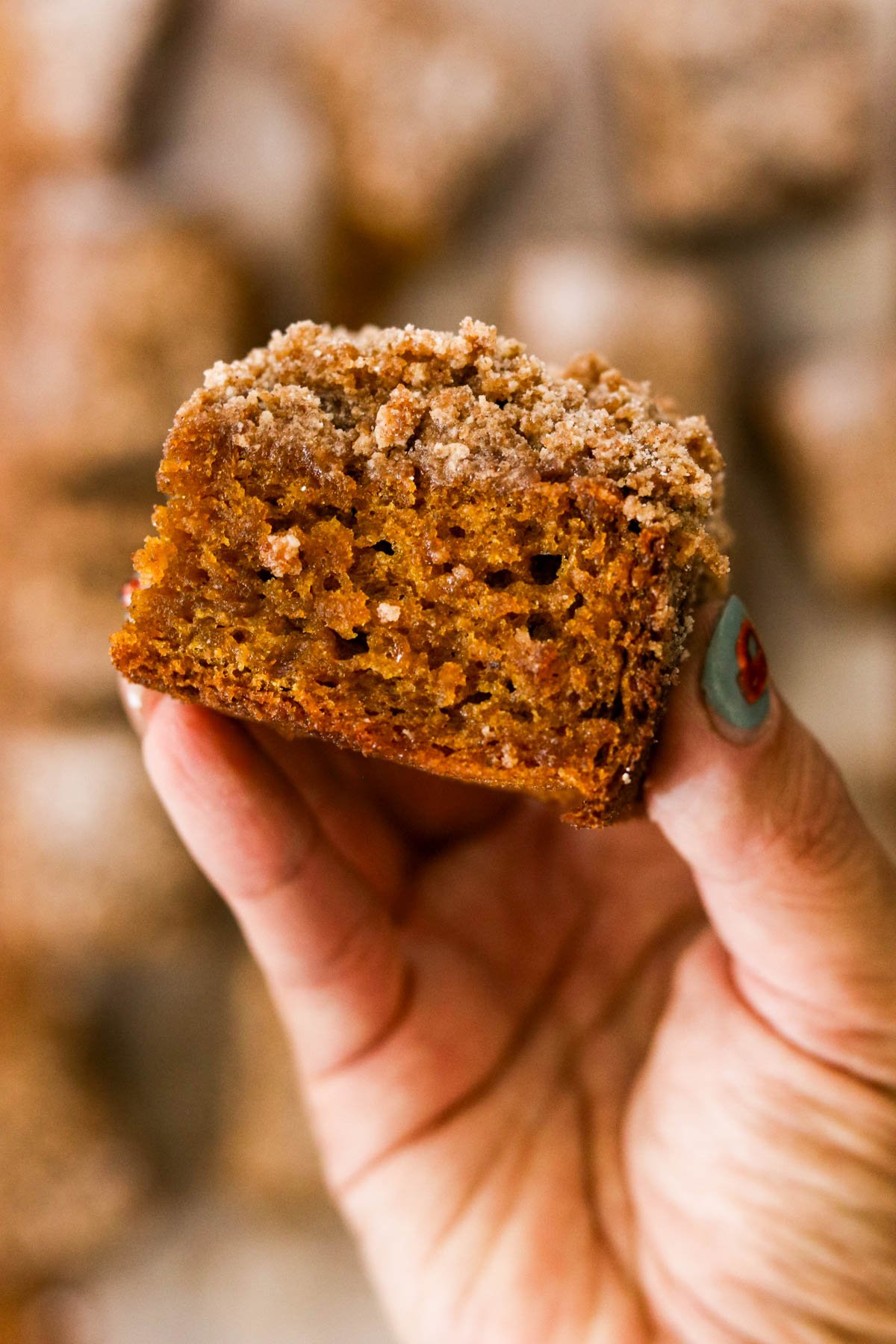 Close-up of a hand holding a slice of pumpkin coffee cake with crunchy cinnamon streusel.