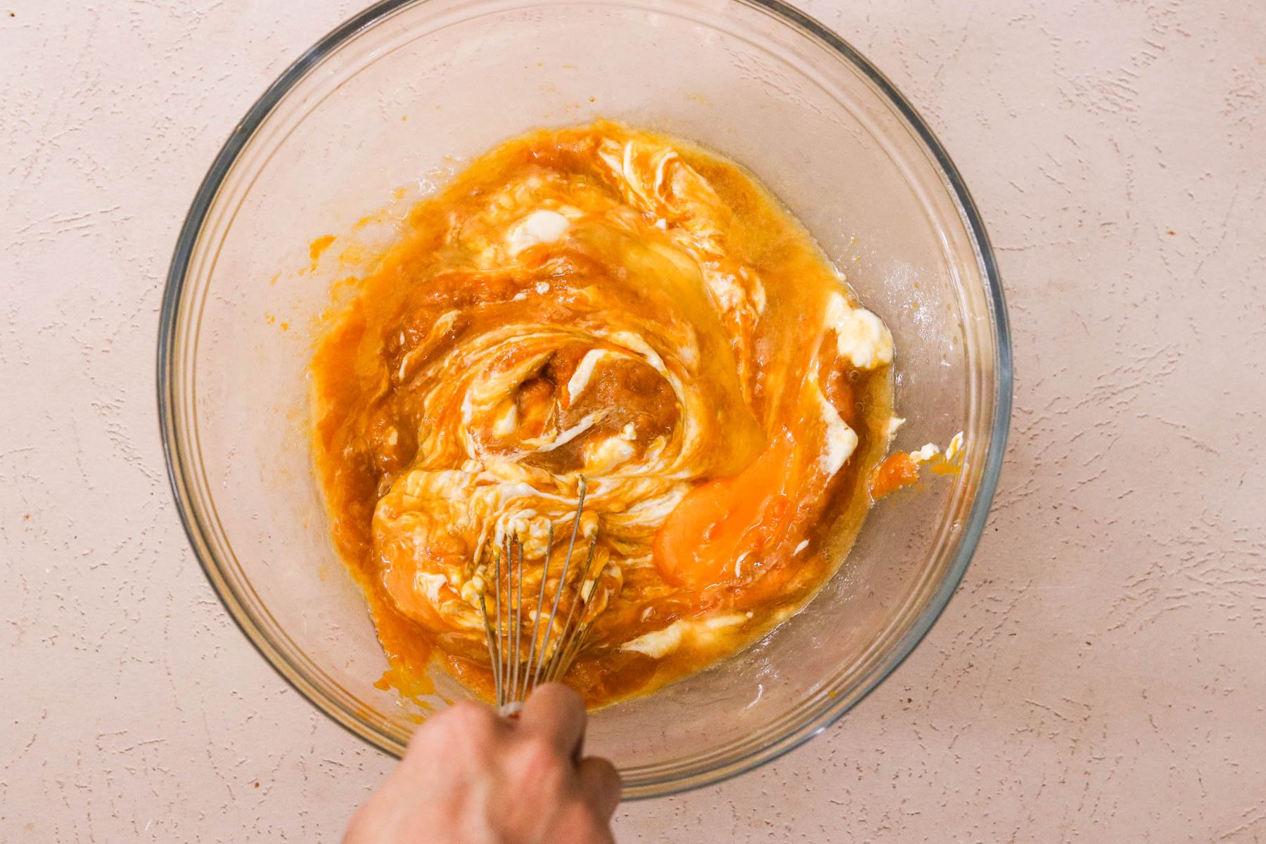 Wet ingredients—pumpkin puree, Greek yogurt, egg, melted butter—whisked together in a glass mixing bowl.