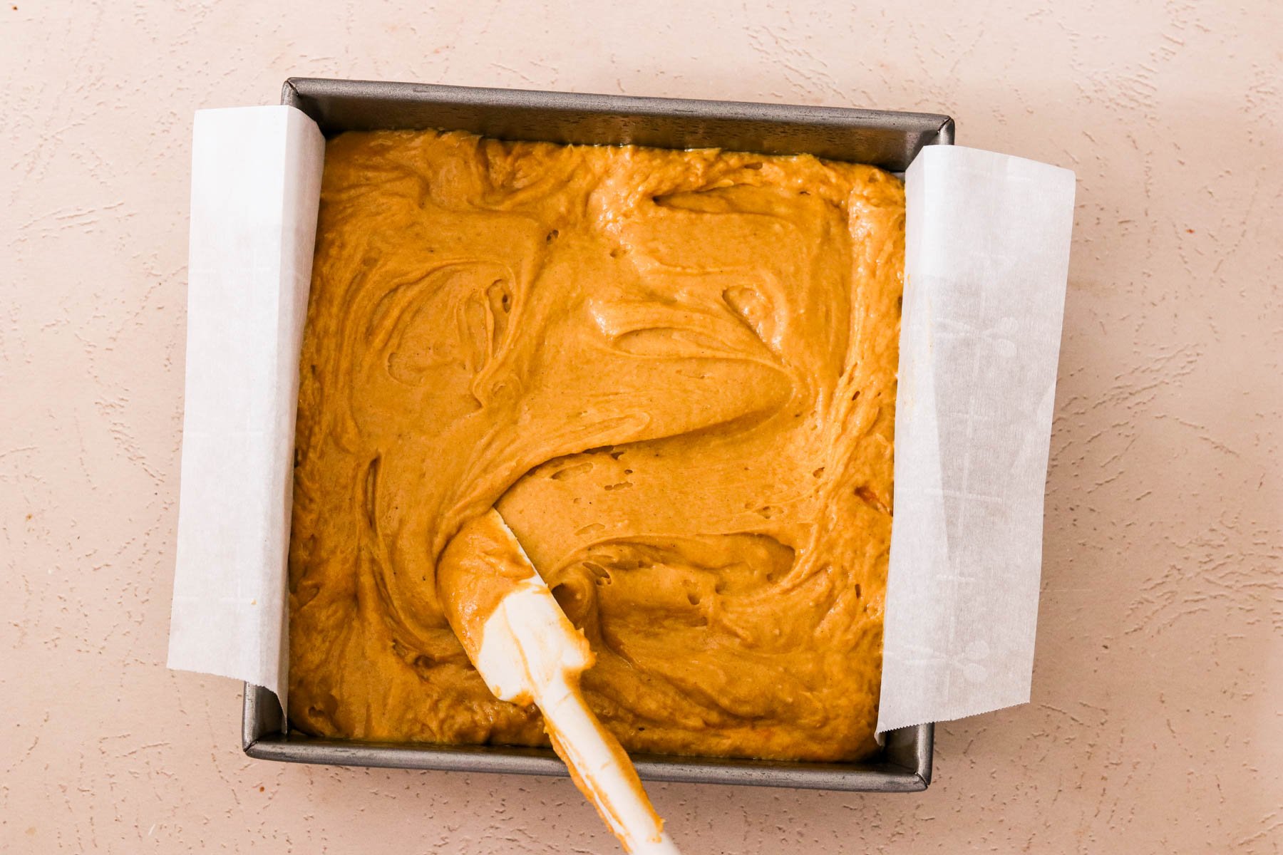 Pumpkin coffee cake batter spread evenly in a parchment-lined 8x8 pan.