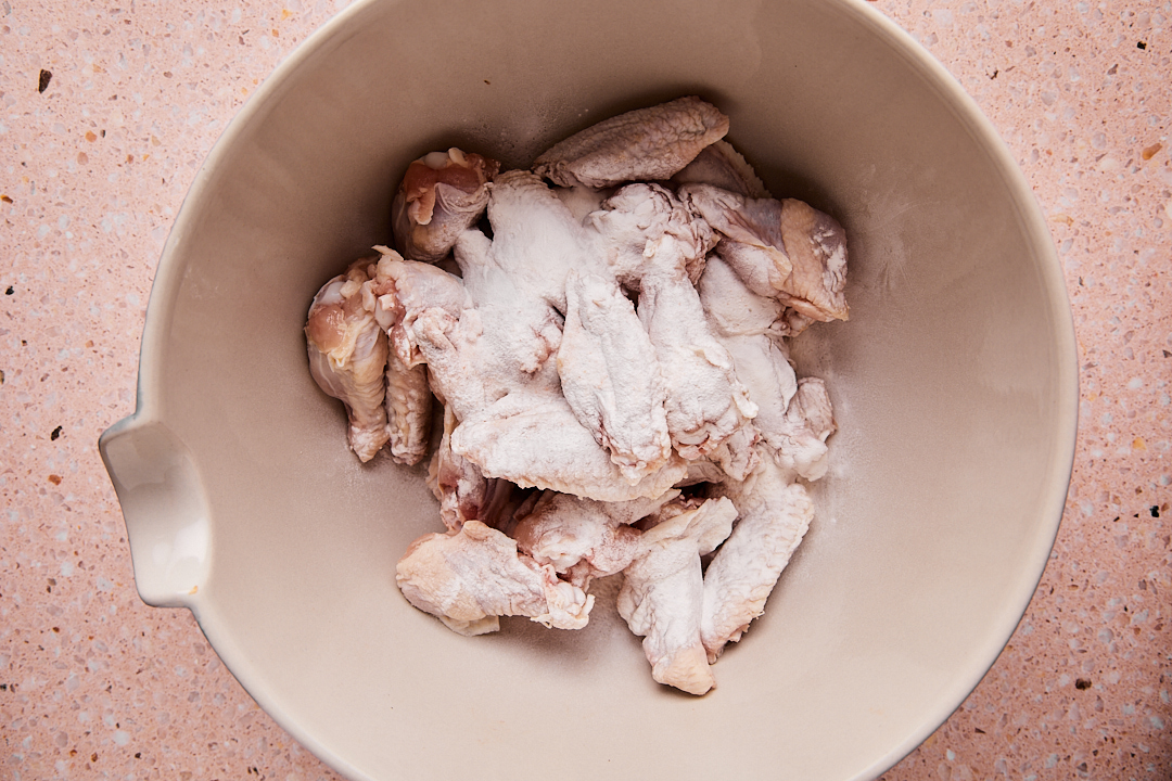 Chicken wings in a light colored mixing bowl sprinkled with baking powder and salt.