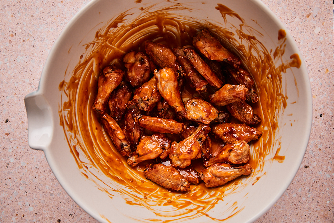 Baked chicken wings in a large bowl coated in the honey sriracha sauce.