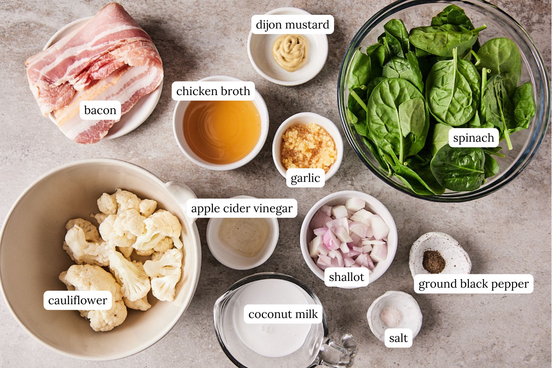 Ingredients for keto creamed spinach labeled and laid out on a gray countertop.