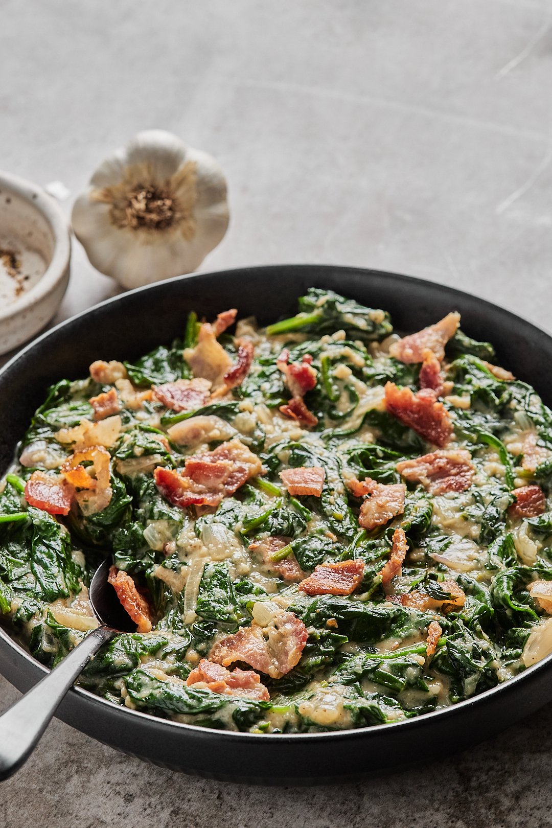 Keto creamed spinach in a black bowl with a spoon in front of a gray background.