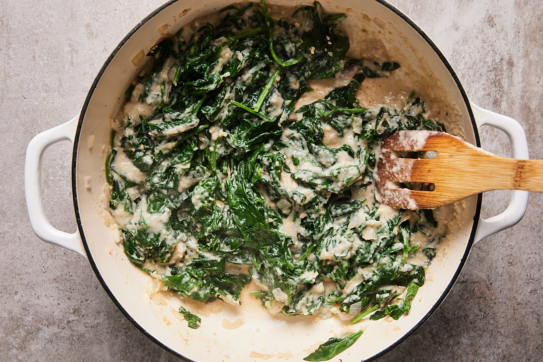 Cauliflower cream sauce being stirred into wilted spinach, shallot, and garlic in large Dutch oven.