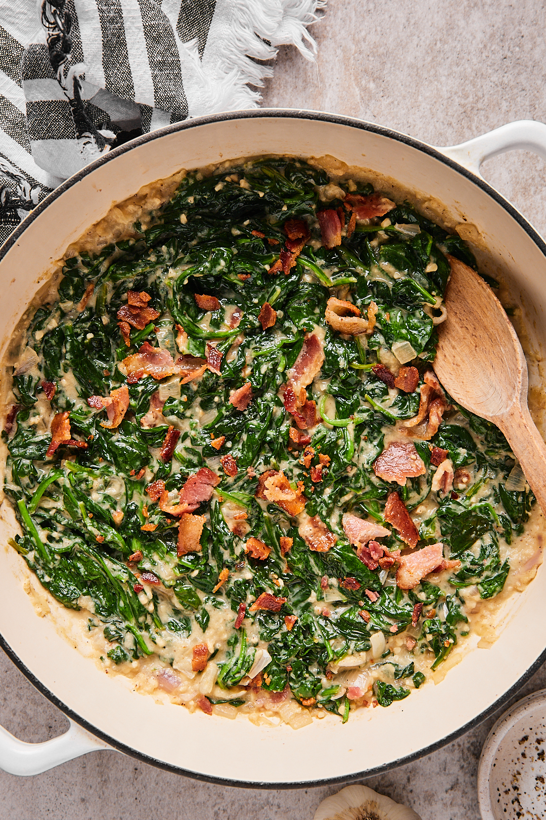 Keto creamed spinach in a white Dutch oven with a wooden spoon.