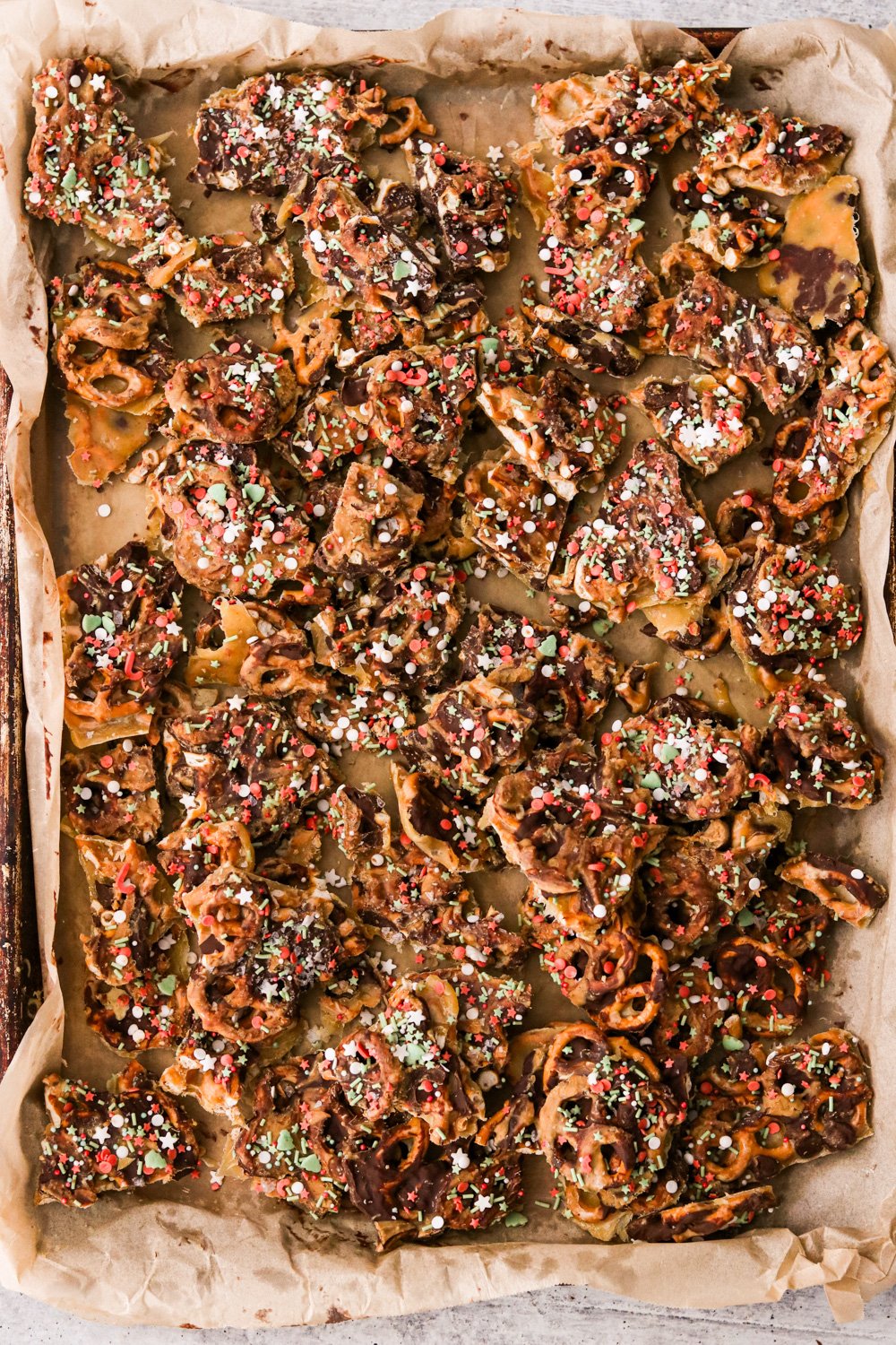 christmas crack with pretzels on a baking sheet covered in chocolate, sprinkles, and sea salt