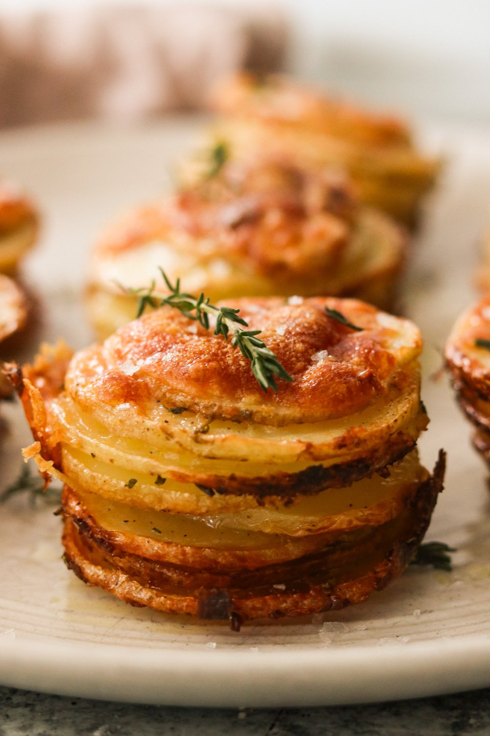Close-up of crispy stacked potatoes on a plate garnished with flaky sea salt and a sprig of thyme.