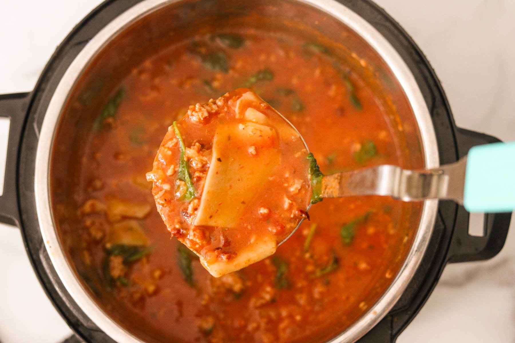 Silver ladle lifting instant pot lasagna soup showing tender lasagna noodles and wilted spinach. 