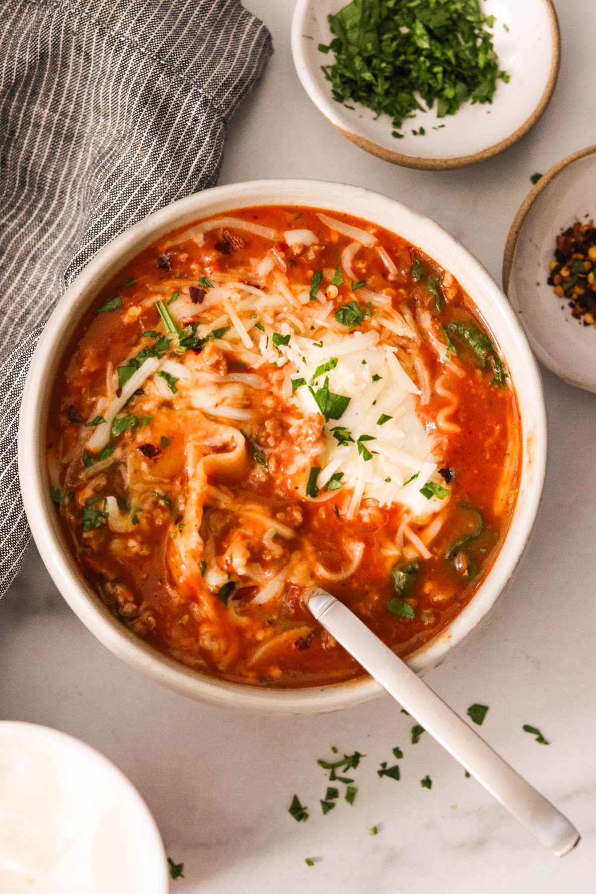 Instant Pot lasagna soup in a bowl, topped with melted cheese and fresh herbs, with a spoon ready to eat.