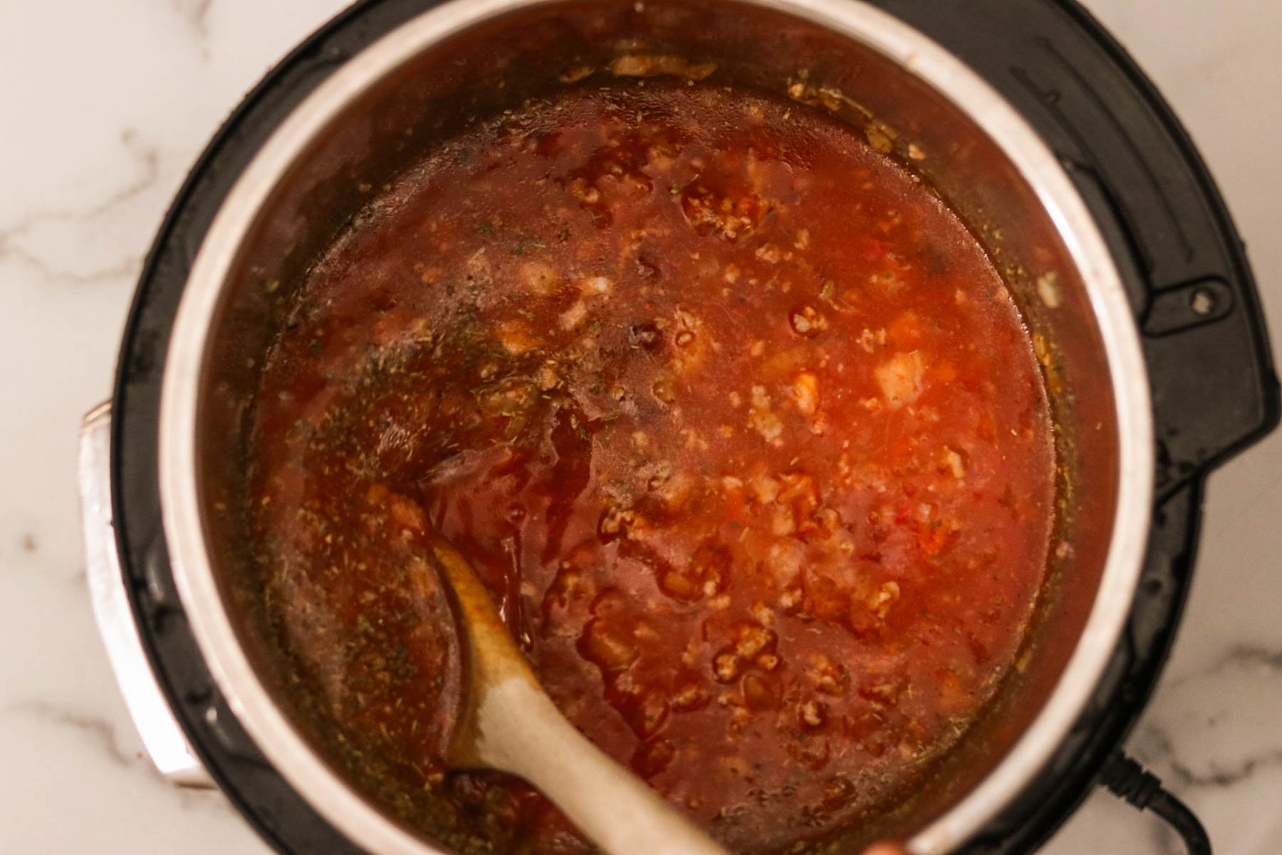 Instant Pot filled with sautéed ground beef and onions simmering in broth, marinara sauce, and Italian seasoning.