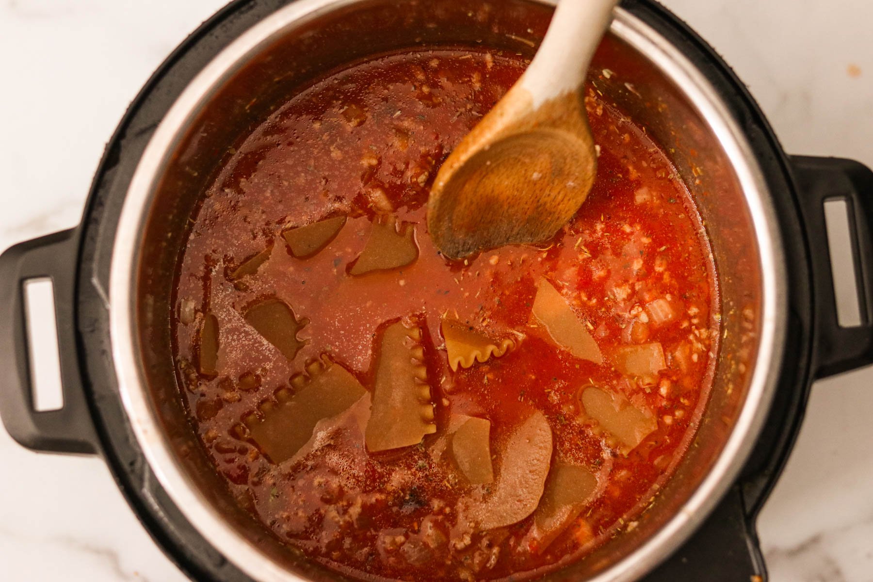 Broken pieces of lasagna noodles in the Instant Pot with sautéed onion and beef and the broth mixture.