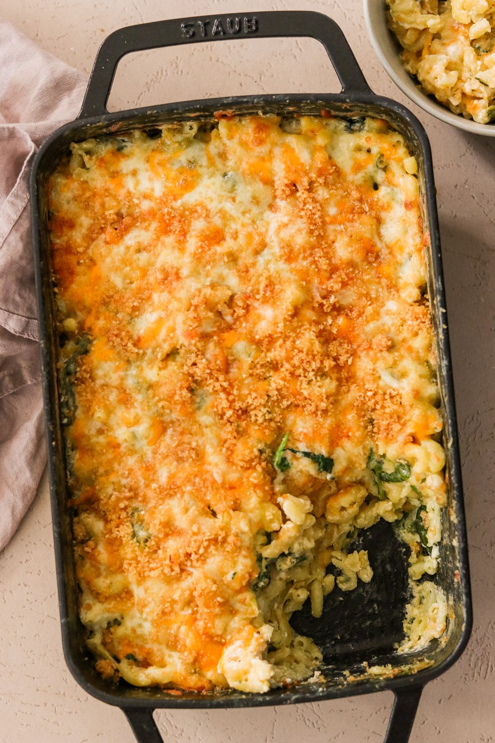 Spinach and artichoke mac and cheese in a black STAUB 9x13 pan with one corner piece removed.
