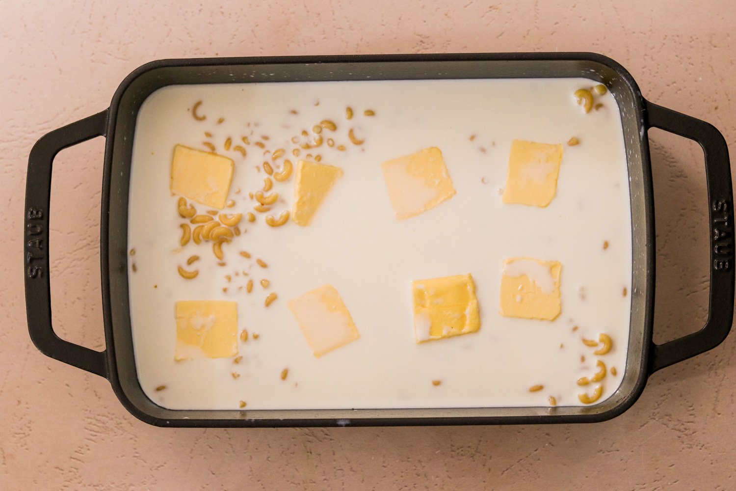 Sliced butter in a 9x13 pan with pasta, milk, and sea salt.
