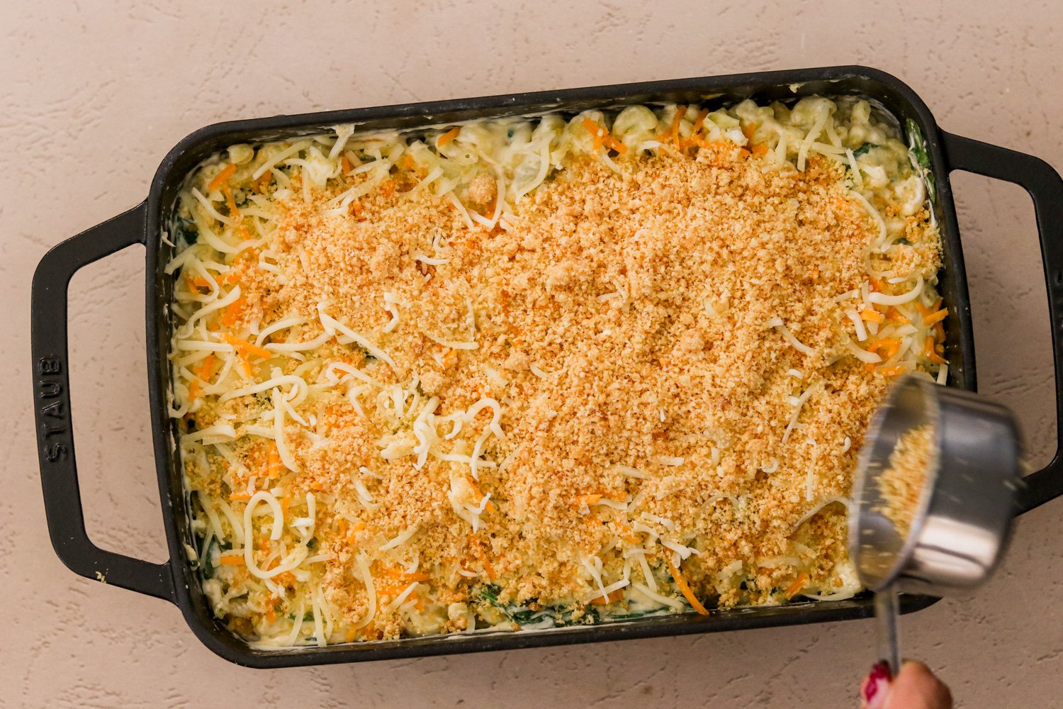 Pasta mixture in a baking dish with cheese and cubed cream cheese stirred into a smooth sauce, then topped with more cheese and breadcrumbs.