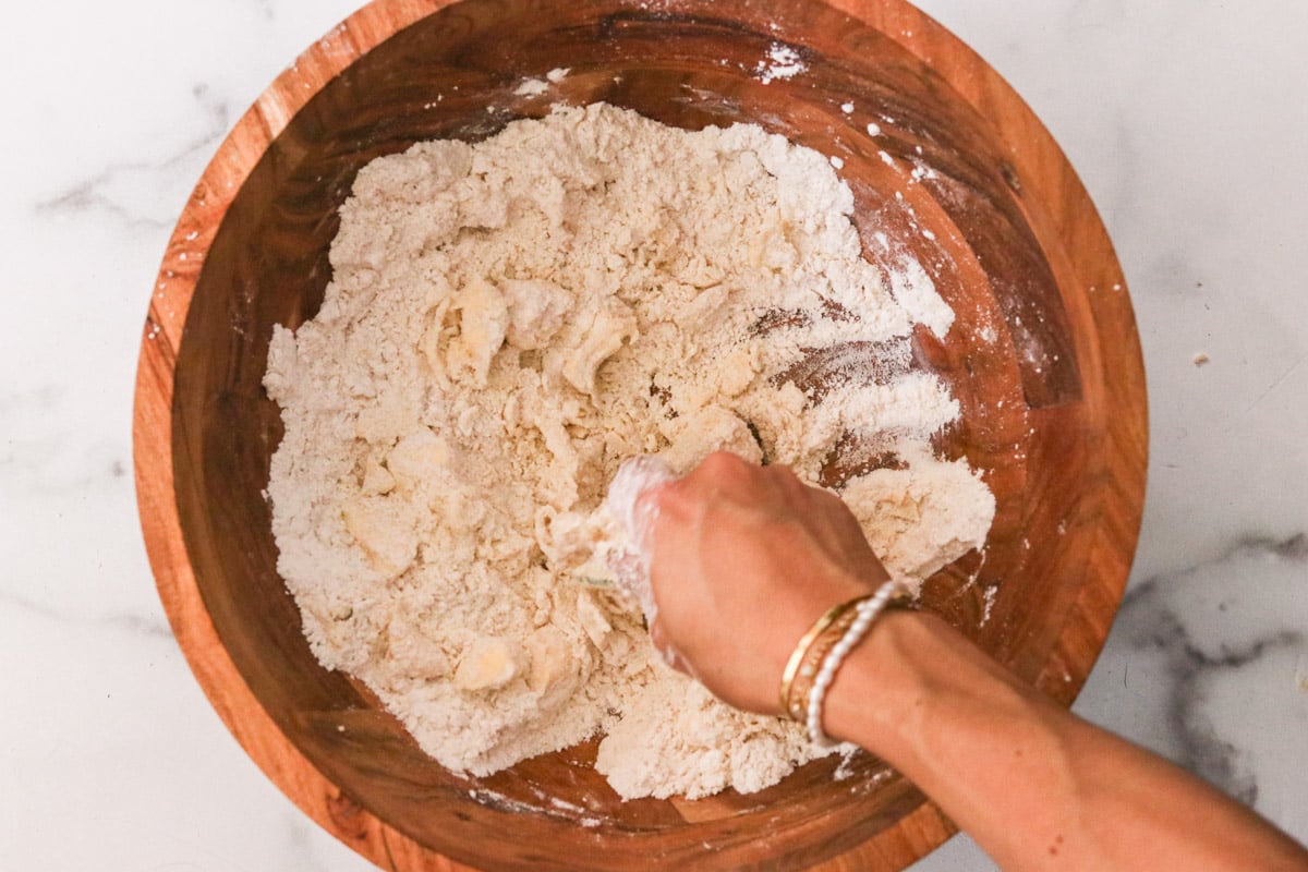 Cold butter being cut into the dry ingredients with a hand tool creating pea-sized crumbs.