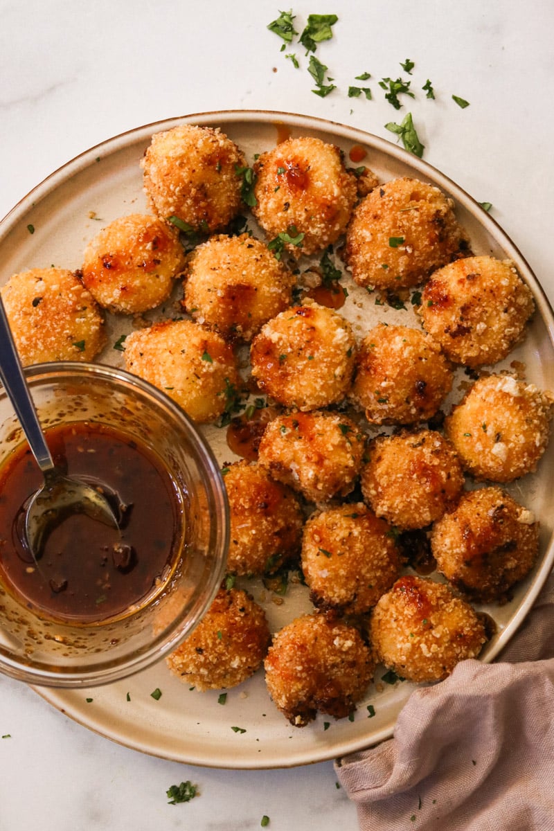 Fried goat cheese balls on a plate, drizzled with honey and topped with flaky sea salt and chopped parsley.