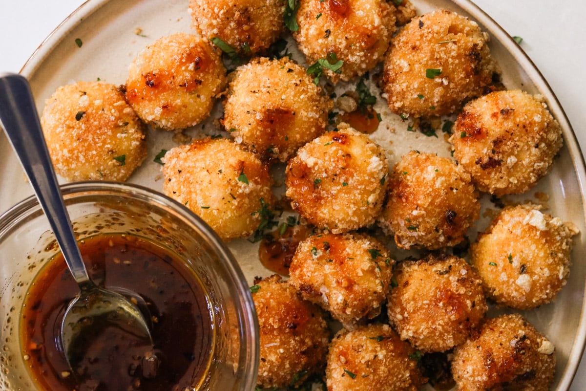 Fried goat cheese balls on a plate, drizzled with honey and topped with flaky sea salt and chopped parsley.
