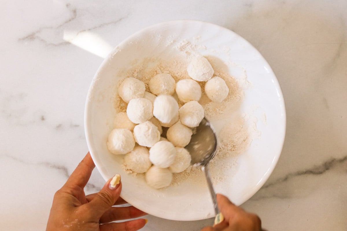 Goat cheese balls in a bowl, tossed and coated evenly in flour.