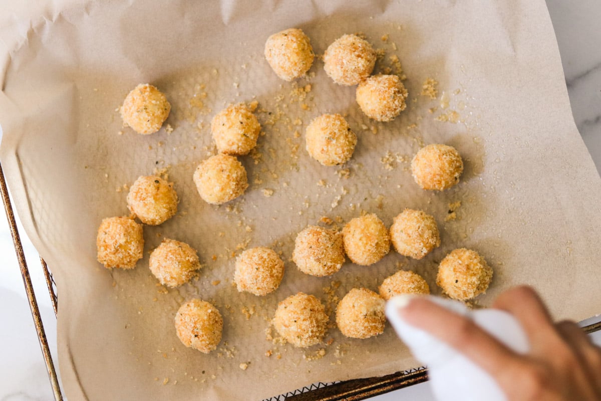 Goat cheese balls being sprayed with cooking spray.