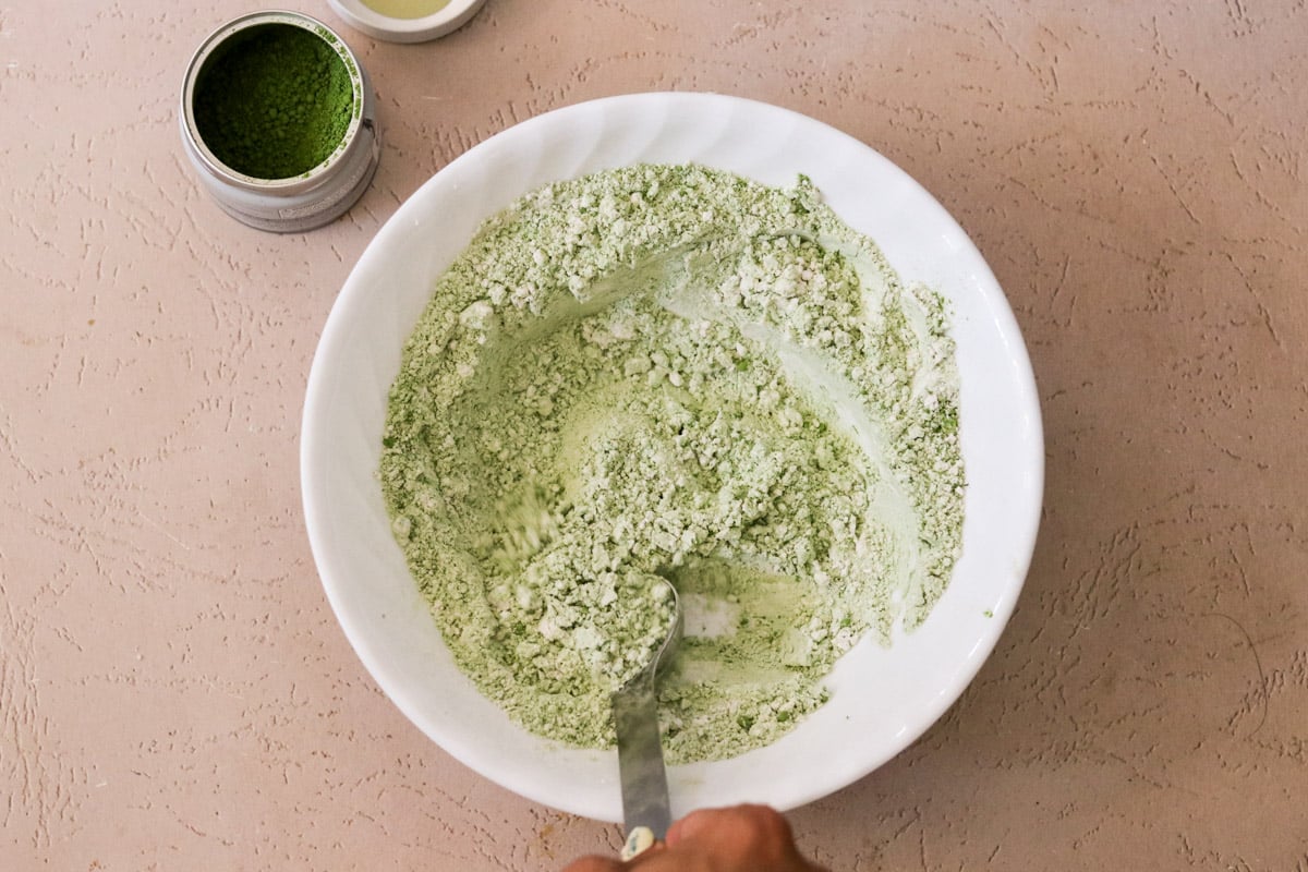 A shallow bowl with flour, matcha powder, baking soda, and salt.