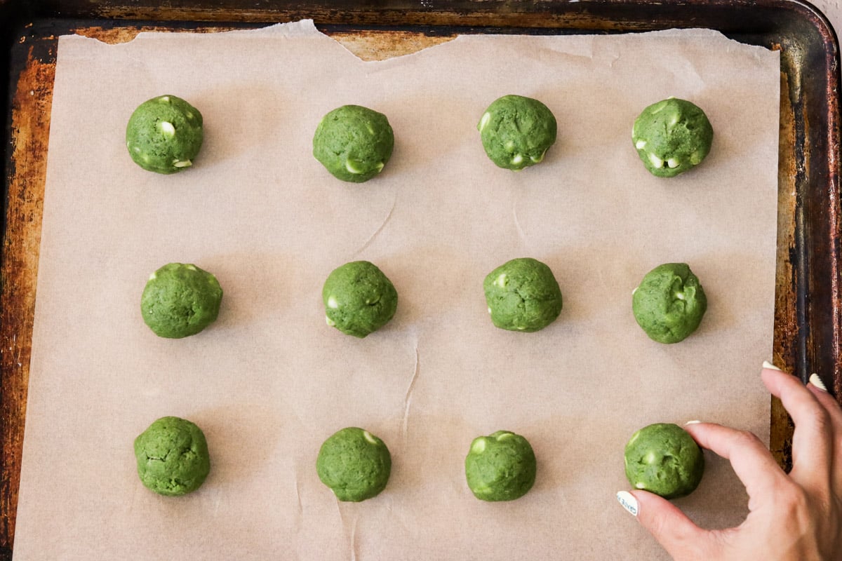 Matcha chocolate chip cookie dough rolled into balls on a parchment lined baking sheet.