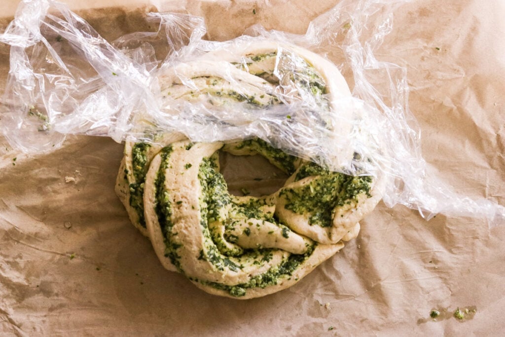 the two ends of the braided dough wreath connected and covered with plastic wrap to rise