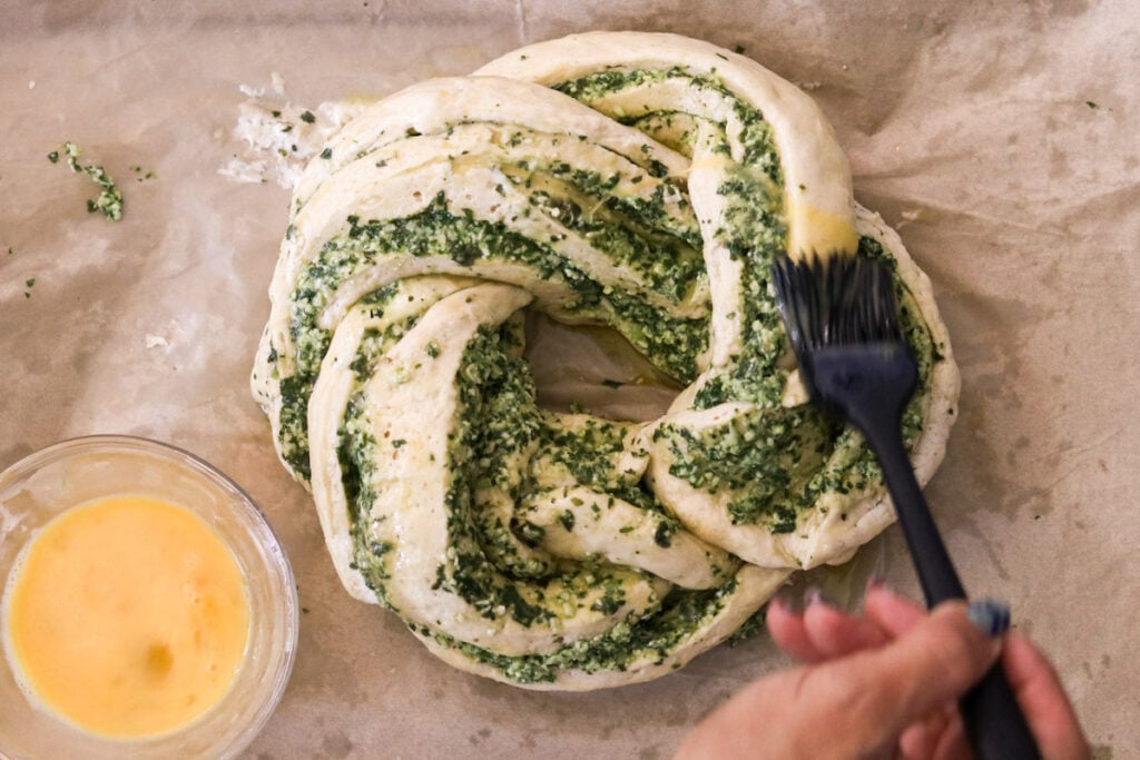 brushing the wreath bread with an egg wash before baking