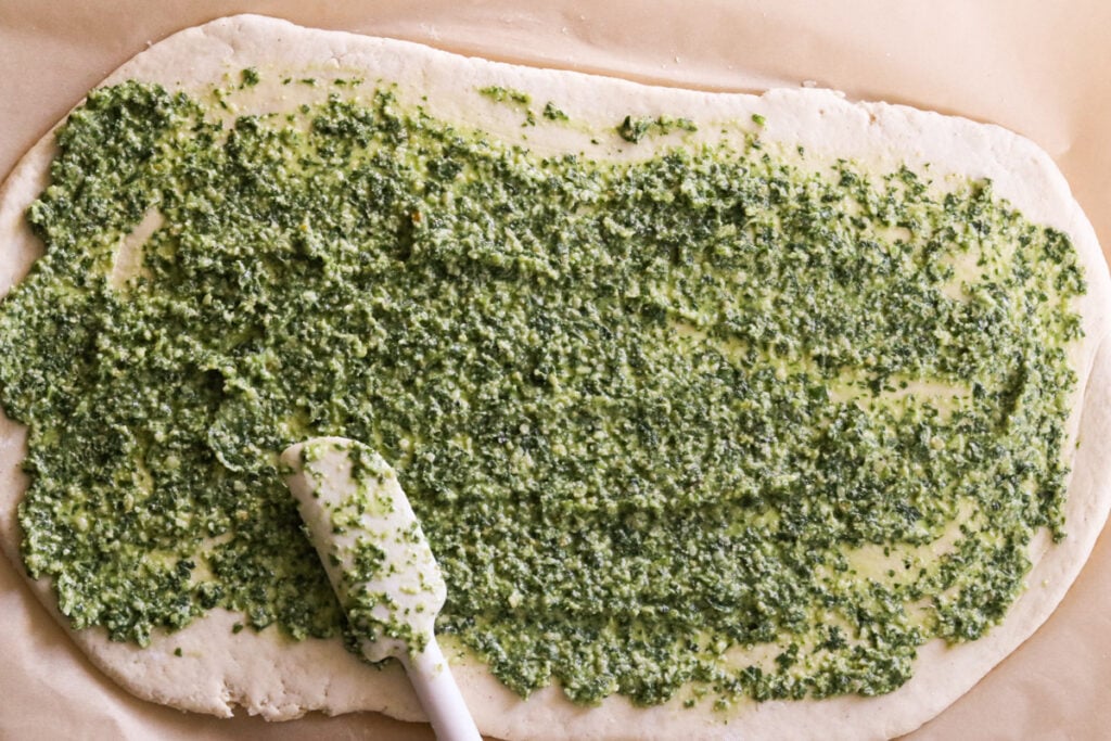 spreading pesto atop the bread dough before twisting into the bread wreath