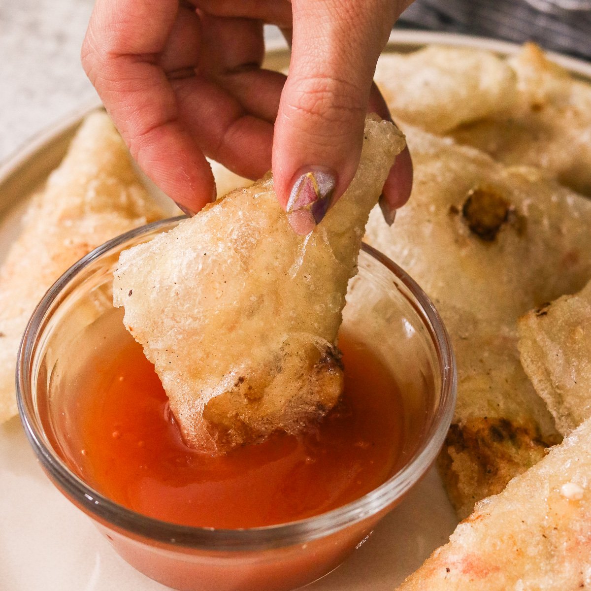 Hand dipping a gluten-free crab rangoon into a bowl of homemade sweet and sour sauce.