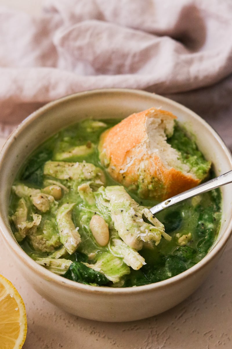 Creamy chicken and white bean soup in a bowl with a piece of crunchy bread and a spoon resting inside.