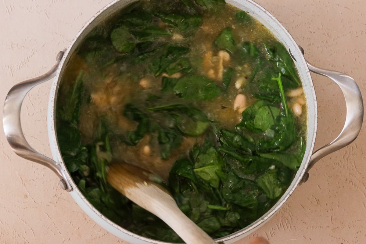 Beans and spinach added to the large soup pot with chopped, sautéed onion, garlic, seasonings and chicken broth.
