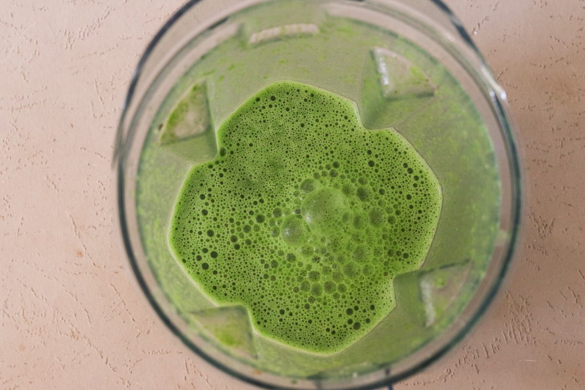 An immersion blender, with blended green soup in it.
