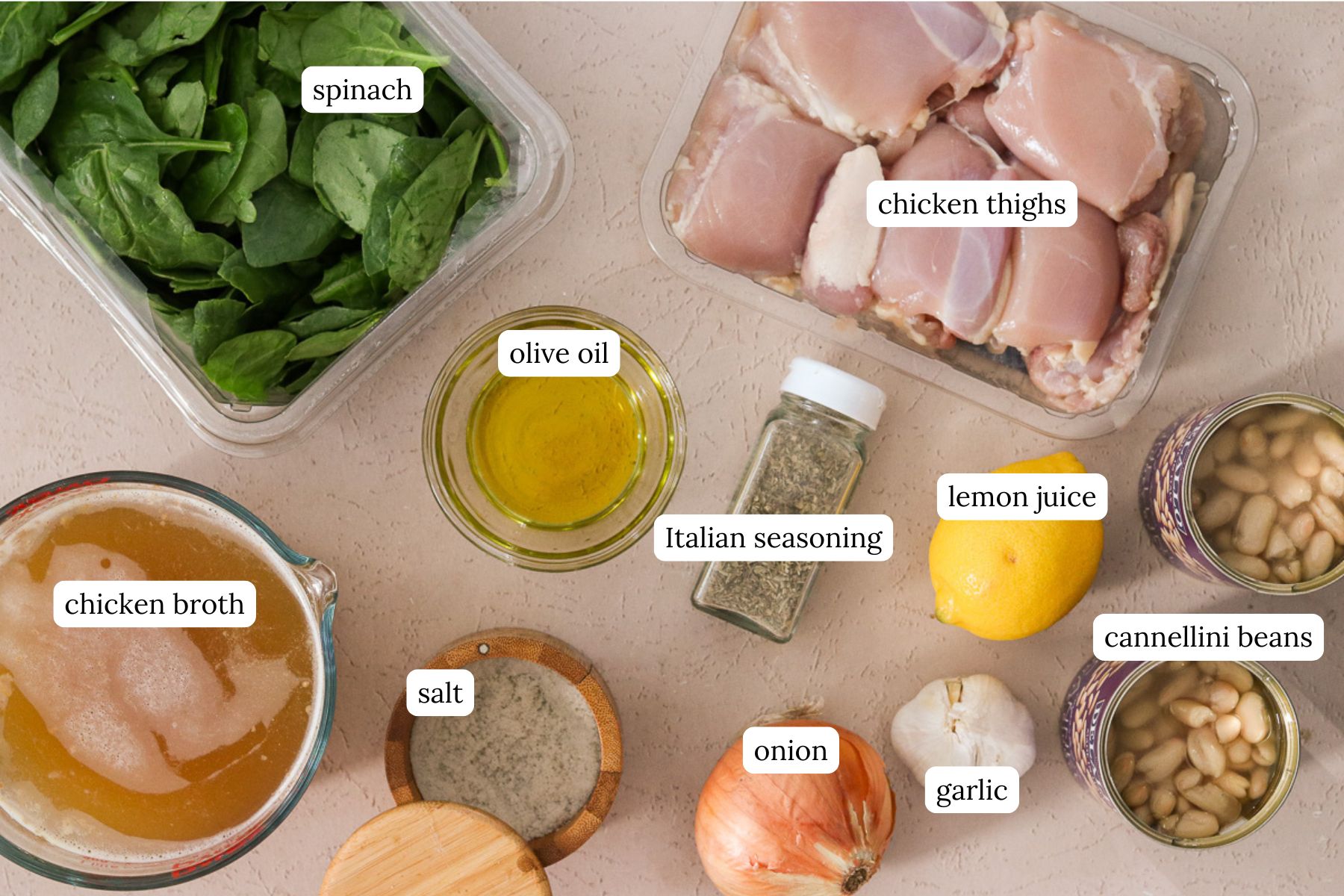 Ingredients for creamy chicken and white bean soup labeled and laid out on a light colored countertop.