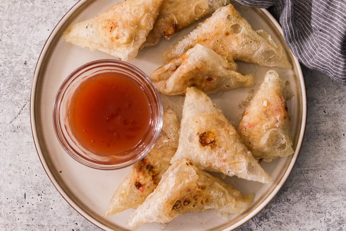 Gluten-free crab rangoon served on a plate with a small bowl of sweet and sour sauce.