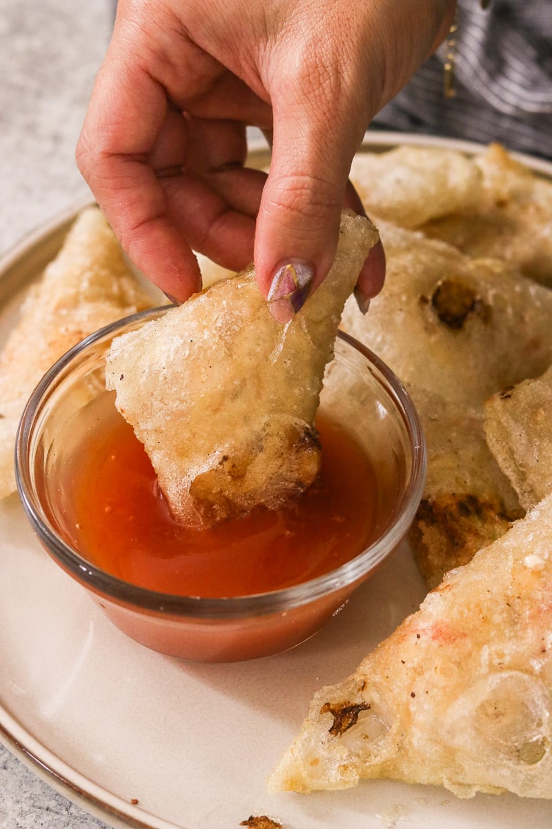 Hand dipping a gluten-free crab rangoon into sweet and sour sauce.