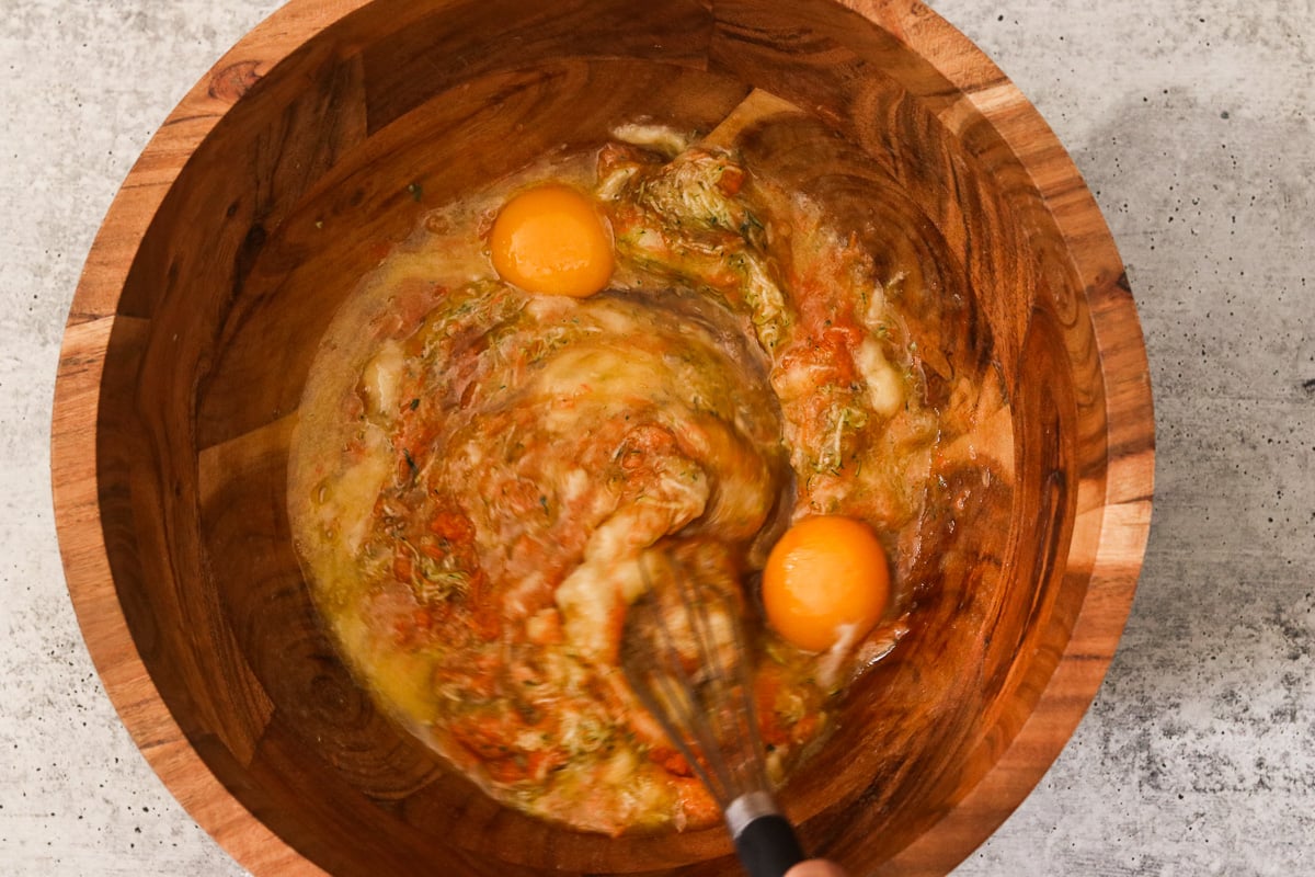 A large wooden bowl with zucchini, carrot, apple, banana, butter, honey, eggs, and vanilla extract.
