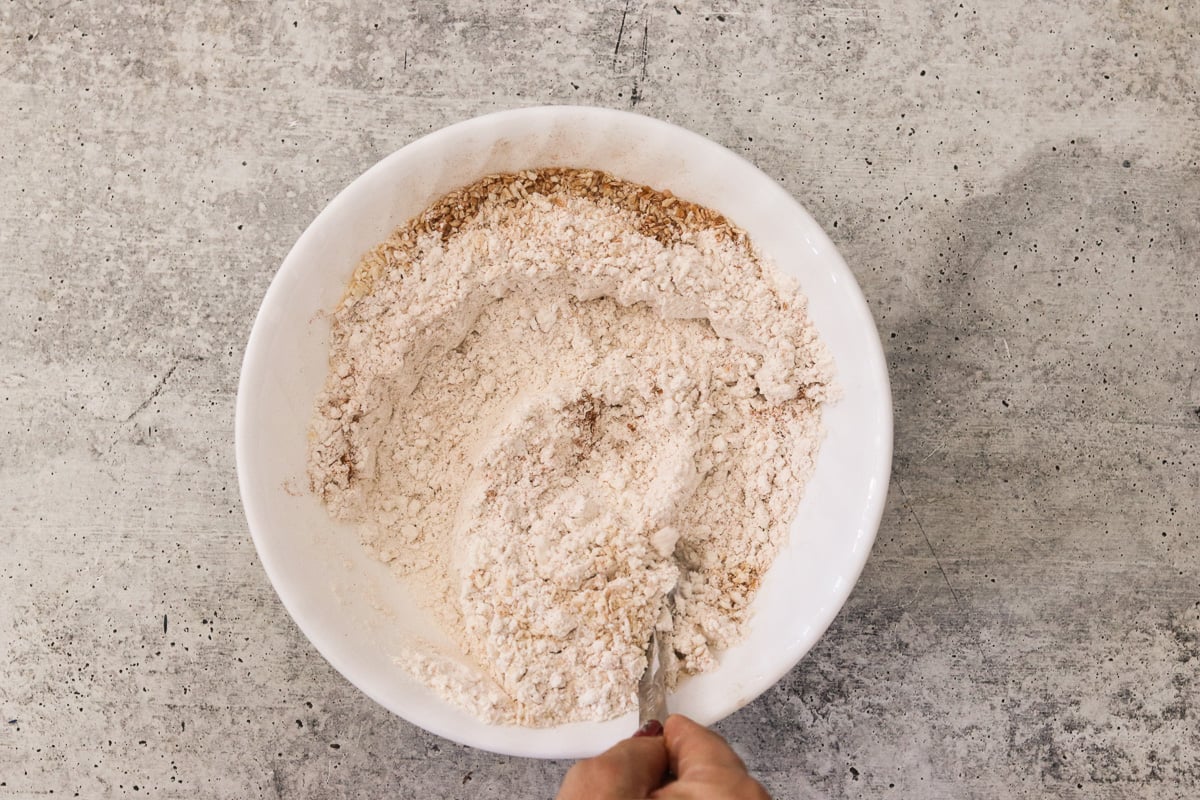A white bowl with gluten-free flour, coconut flakes, baking soda, cinnamon, and sea salt mixed together.