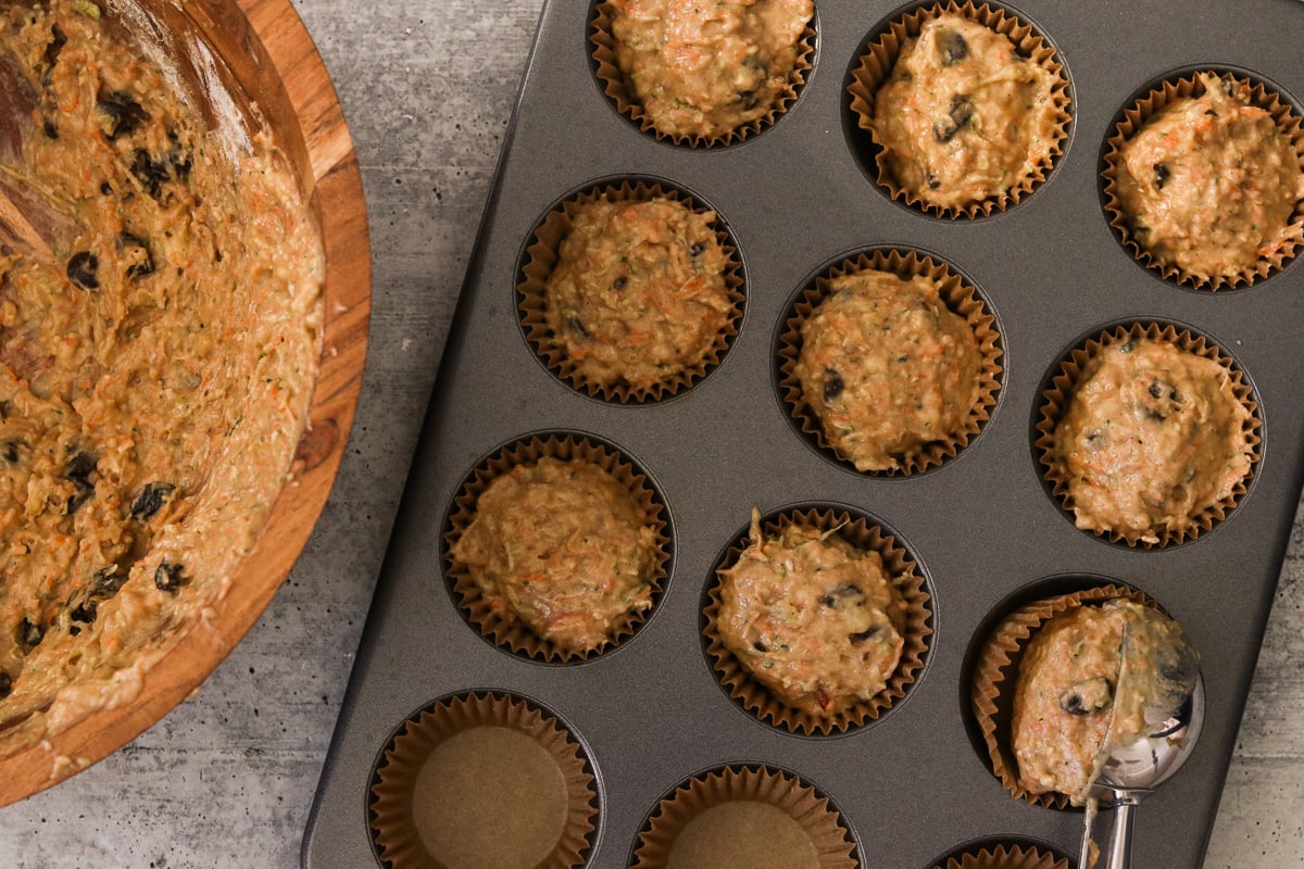 Batter being divided evenly among the muffin cups, filling them almost to the top.