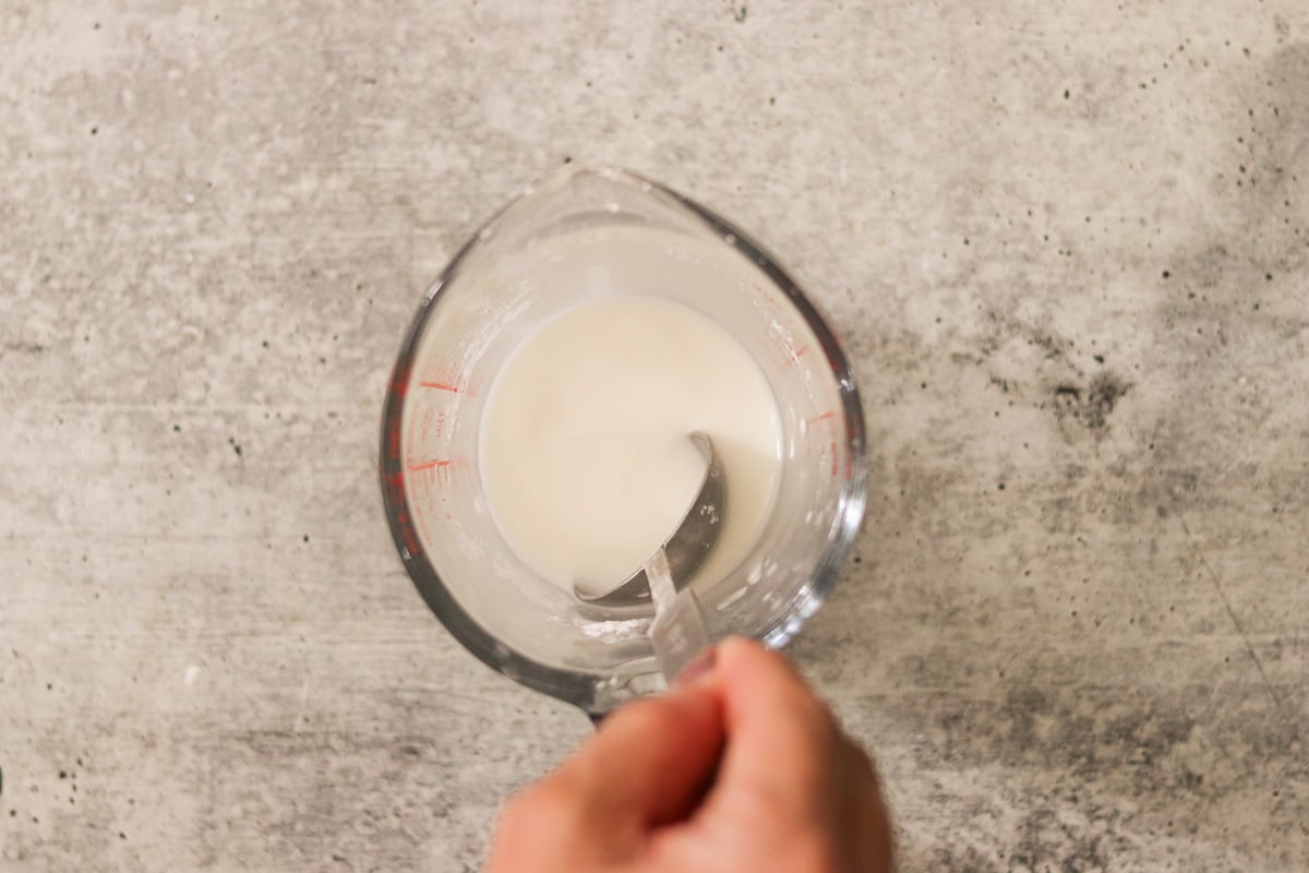 Cornstarch and water being whisked together in a glass measuring cup