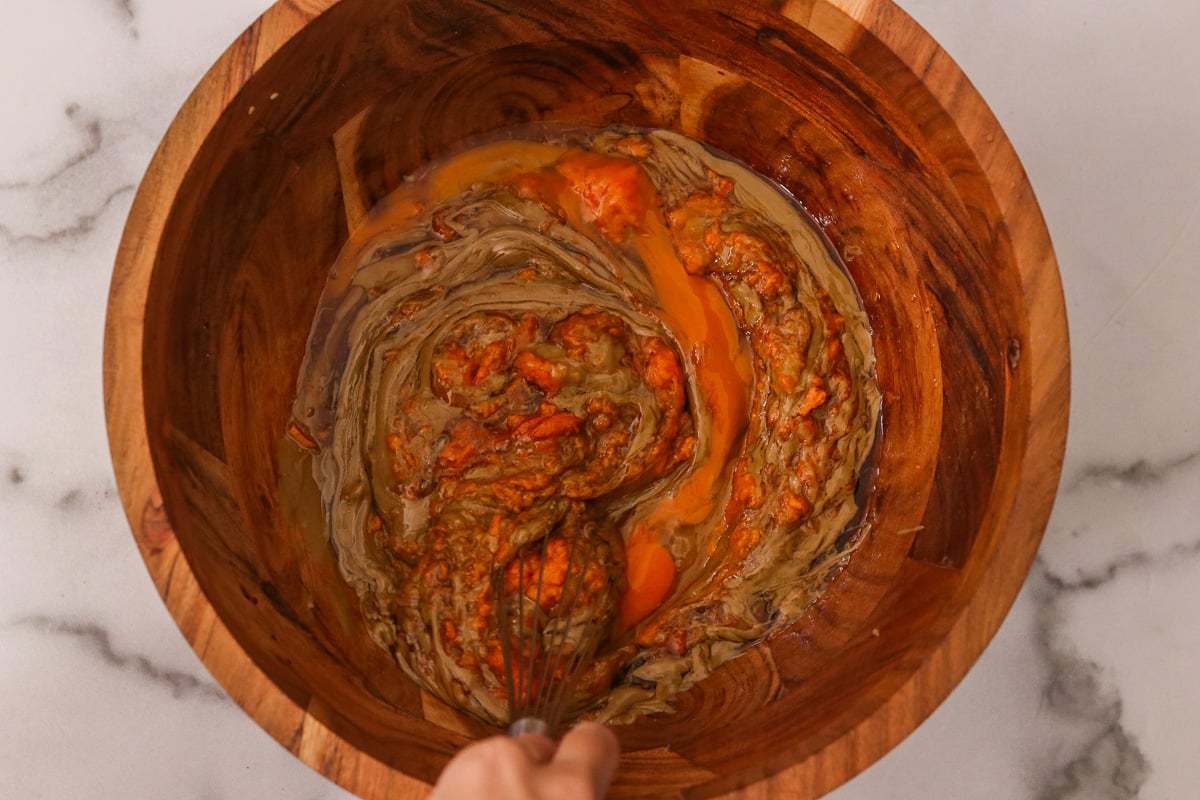 Large wooden bowl with almond butter, sweet potato puree, maple syrup, egg, and vanilla extract.