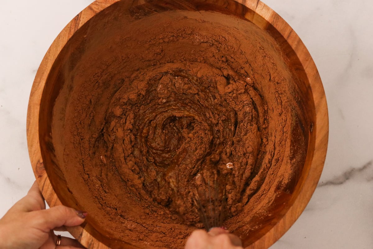 Cocoa powder, baking soda, and sea salt being stirred into the same wooden bowl.