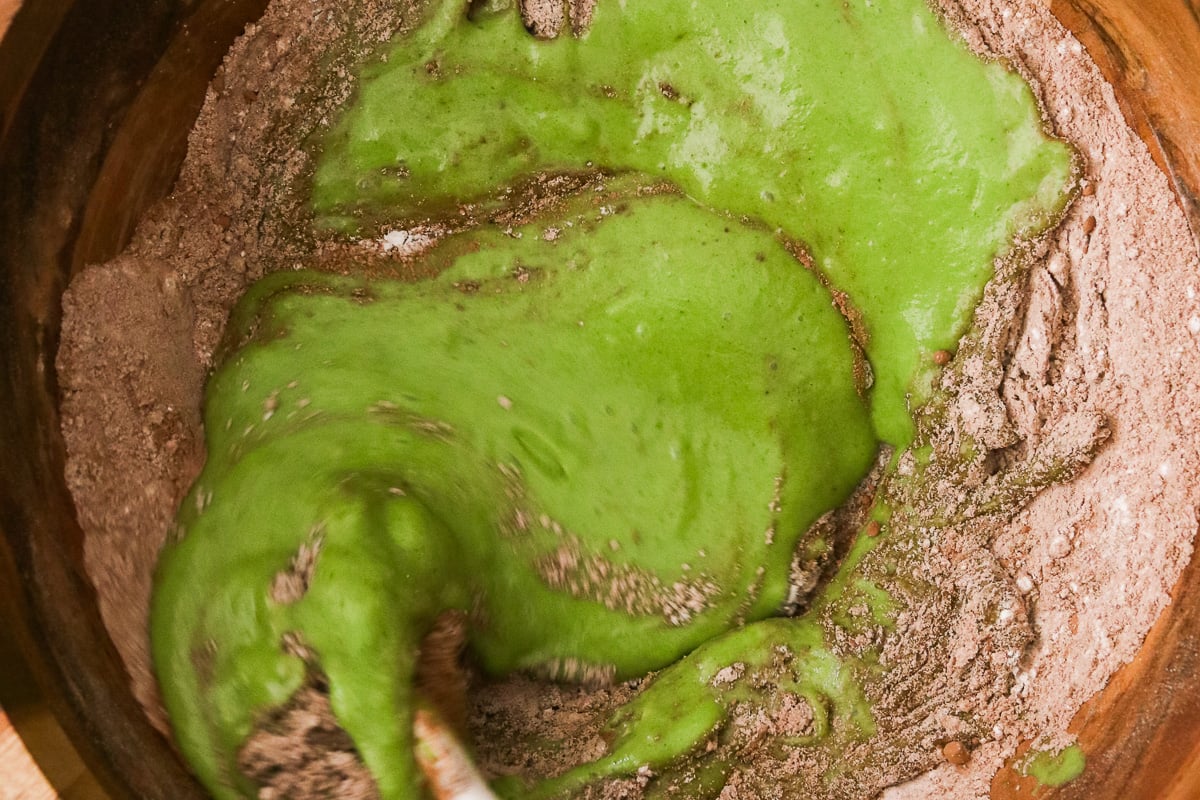 Blended wet ingredients being poured into dry ingredients to make hidden veggie chocolate muffin batter.