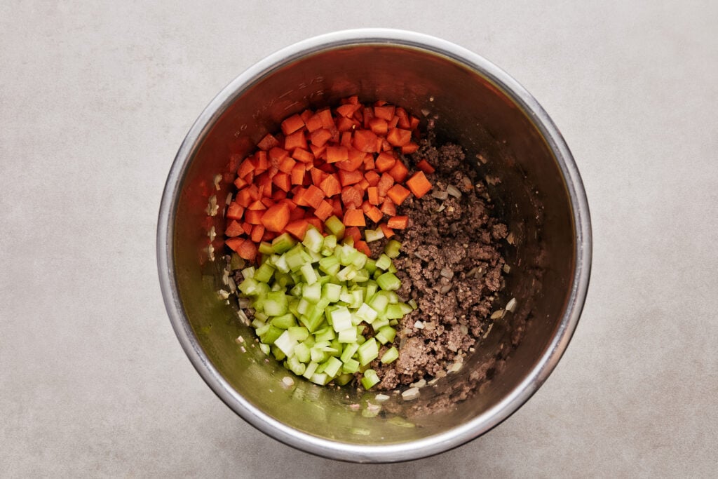 adding veggies to the instant pot with the cooked ground beef, onions and garlic
